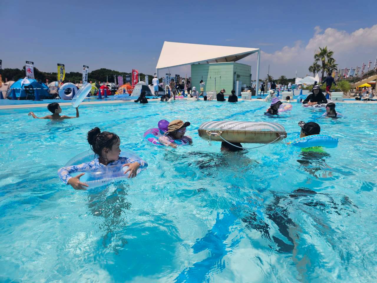 晴れた日に浮き輪で遊ぶ子どもたちとプール全体を広く撮影した写真