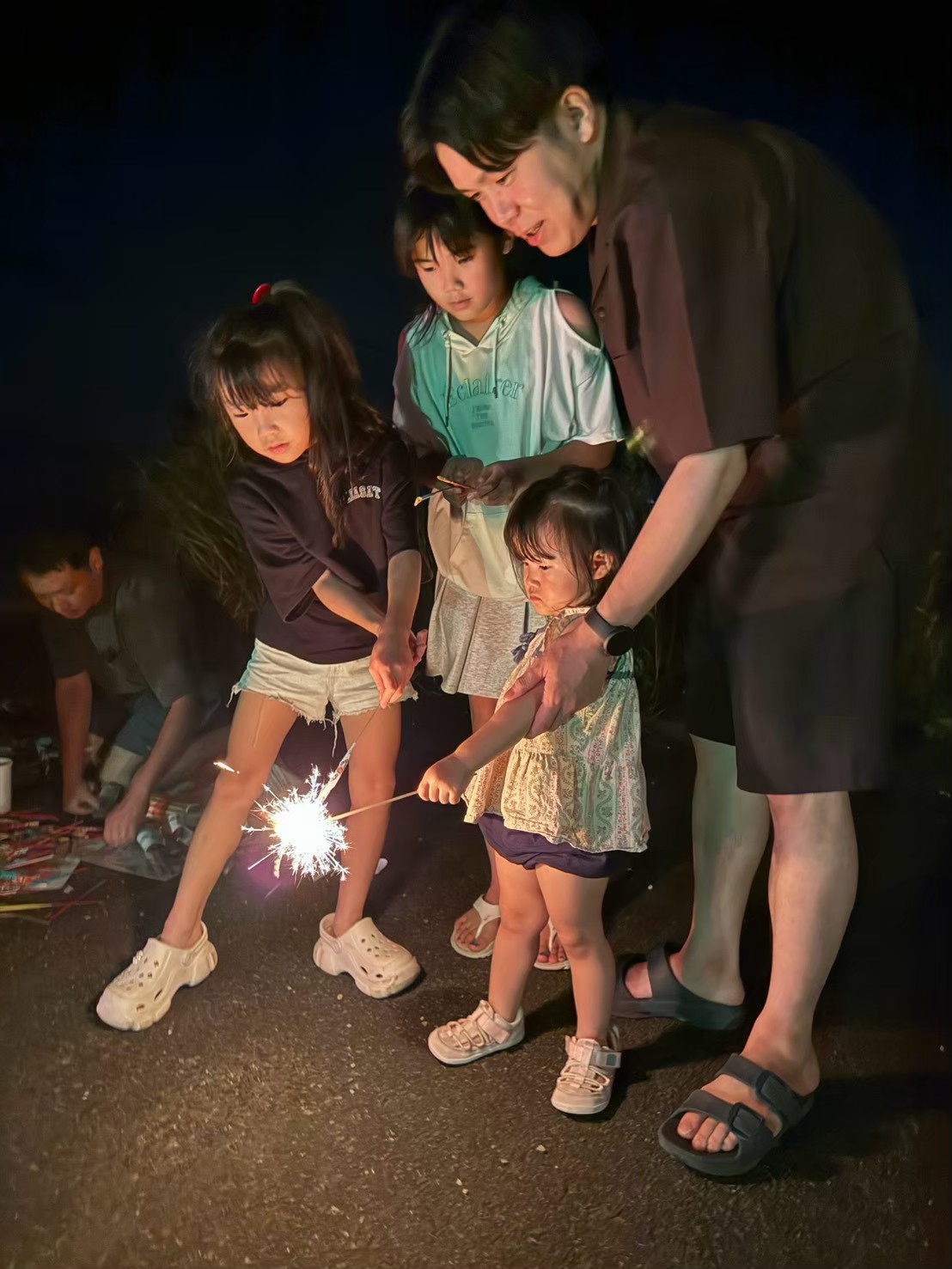 子どもの手元を大人が支えながら花火をする場面